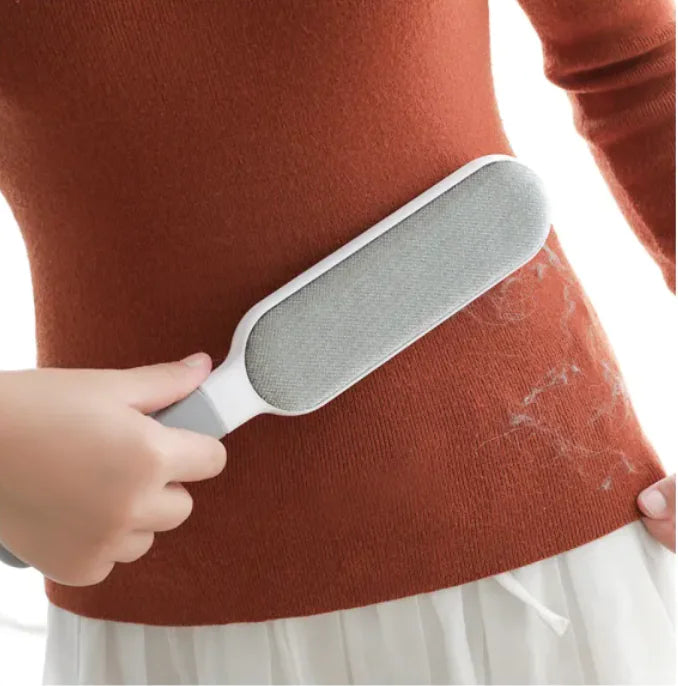 Person using an electrostatic pet hair remover on a sweater with visible hair. 