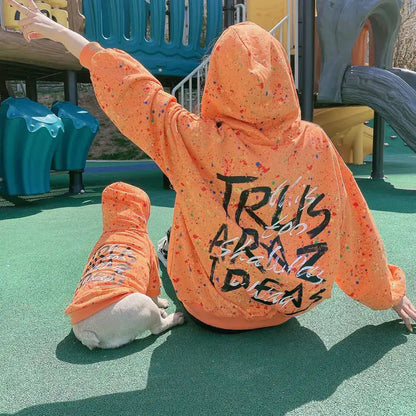 Parent and pet wearing matching Orange (Autumn) hoodies with colorful splatter & text written on the back, twinning for a fun dog walk.