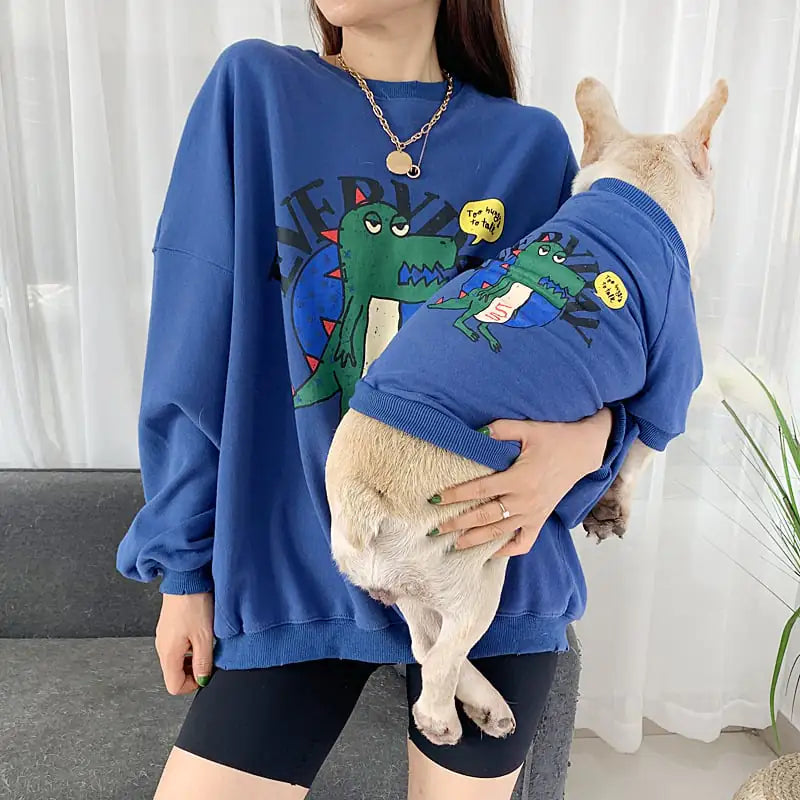 Parent and pet wearing matching Blue (Lake) shirts with a cartoon dinosaur
design, twinning for a fun dog walk.