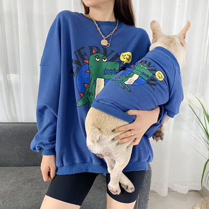 Parent and pet wearing matching Blue (Lake) shirts with a cartoon dinosaur
design, twinning for a fun dog walk.