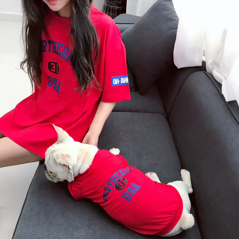 Pet parent and dog relaxing comfortably while wearing matching Red (Ruby) cotton shirts with 'Rortherme USA' text written in blue.
