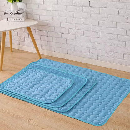 Four Blue (Lake) textured pet sleeping mats of various sizes on a wooden floor with a white brick wall background.