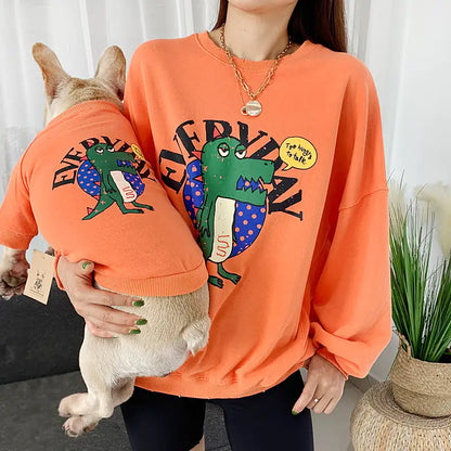 Parent and pet wearing matching Orange (Autumn) shirts with a cartoon dinosaur design, twinning for a fun dog walk.