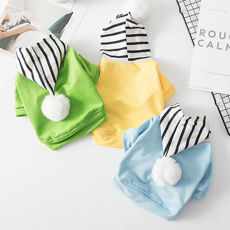 Three polyester dog hoodies with black and white striped hood and white pom-poms in three vibrant colors.