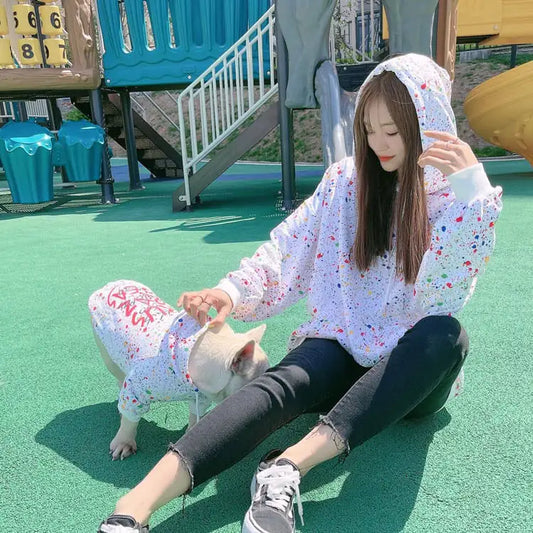 Parent and pet wearing matching White (Pearl) hoodies with colorful splatter & text written on the back, twinning for a fun dog walk.