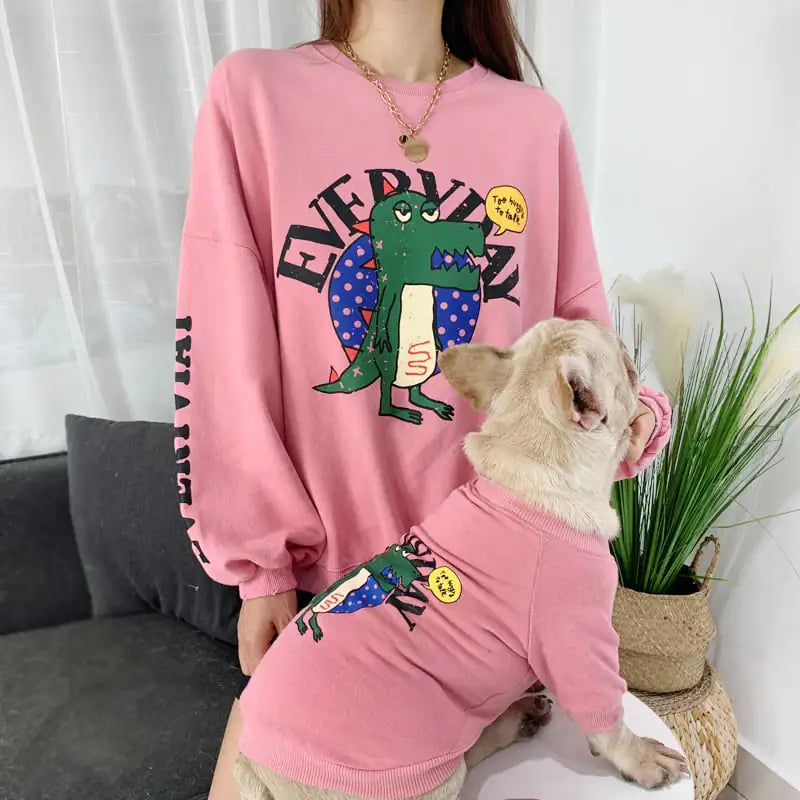 Parent and puppy wearing matching Pink (Rose) shirts with a cartoon dinosaur design, twinning for a fun dog walk.
