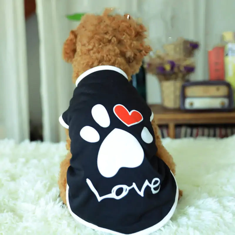 Dog wearing Black (Midnight) shirt with white paw print, red heart, and the word Love on the back, sitting on a blue blanket.