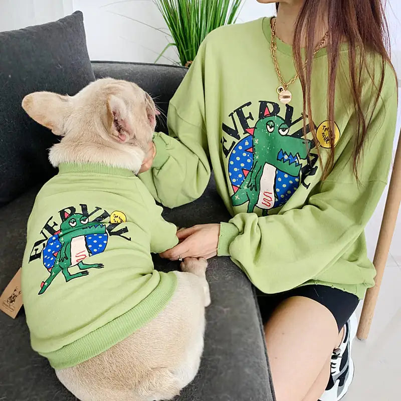 Parent and pet wearing matching Green (Spring) shirts with a cartoon dinosaur design, twinning for a fun dog walk.