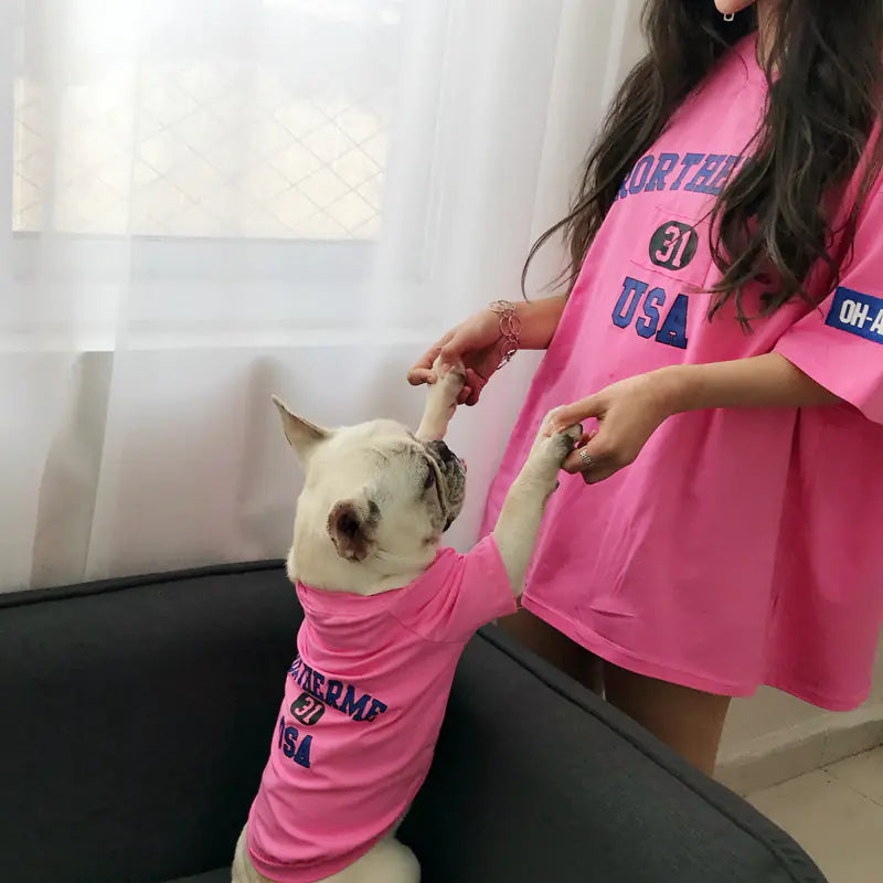 Pet parent and dog playing together while wearing matching Pink (Bubblegum) cotton shirts with 'Rortherme USA' text written in blue.