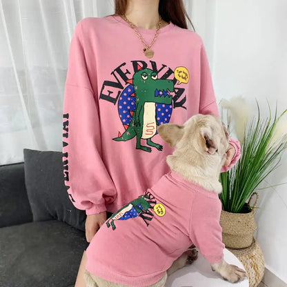 Parent and pet wearing matching Pink (Rose) shirts with a cartoon dinosaur design, twinning for a fun dog walk.